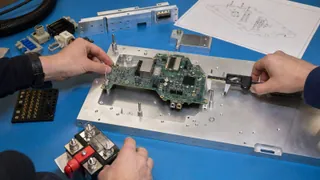 Engineers measuring a circuit board against locating pins and interface hardware while scoping a custom test fixture